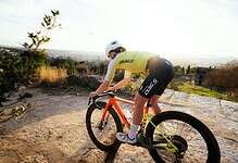 Cyclist riding a mountain bike on rocky terrain with scenic views in the background.
