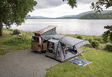 Family camping setup with tent and car near a lake in a scenic outdoor location.