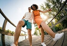 Happy young couple enjoying outdoor walk on a wooden bridge by a lake.